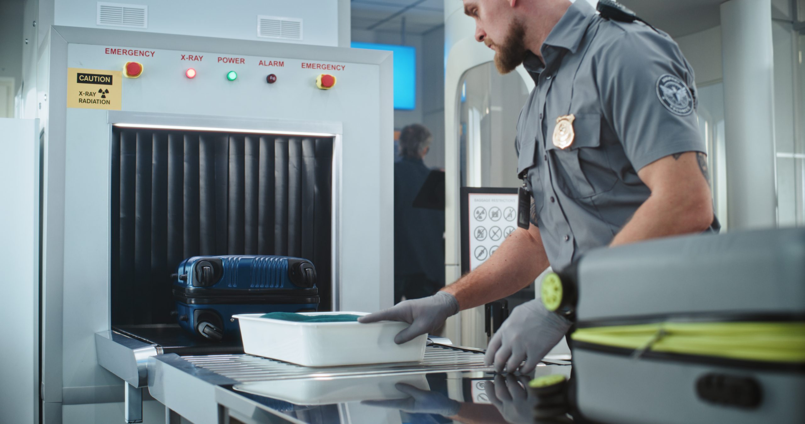 Security Officer Putting Suitcases and Personal Items in Trays on Conveyor Belt with X-ray Scanning Explosives and narcotics detectors are essential devices for ensuring security in critical infrastructures, airports and mass events.